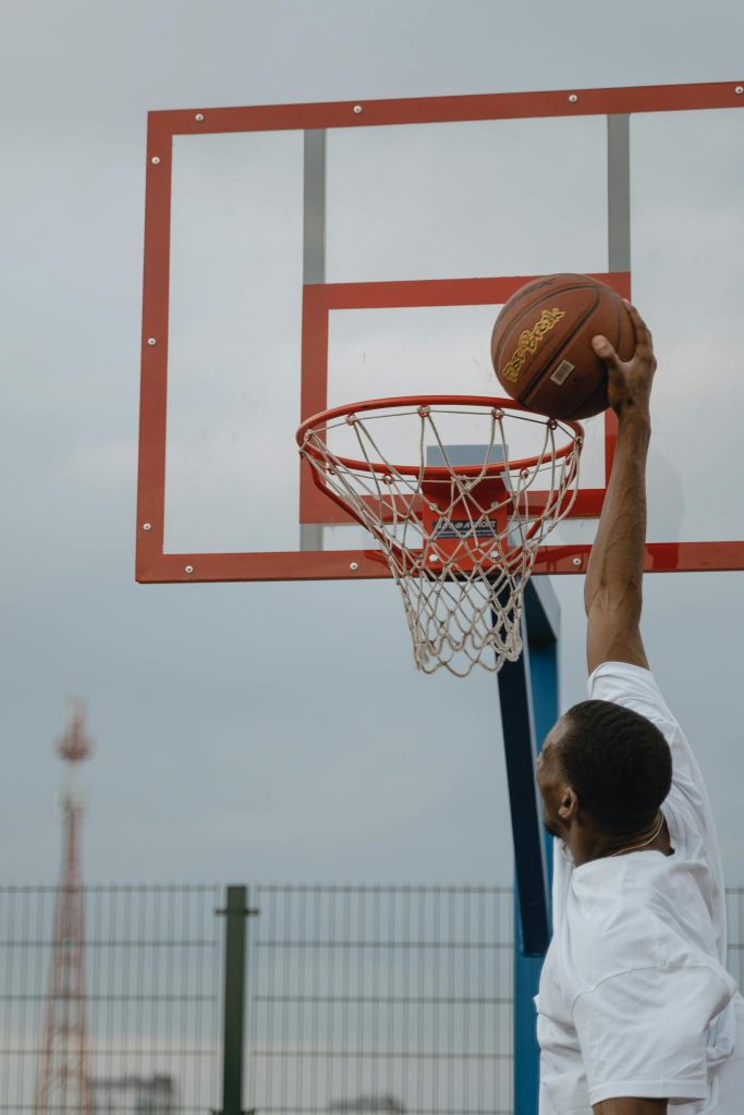 An energetic basketball player dunks on an outdoor court hoop.